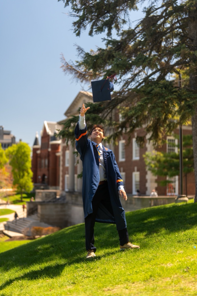 Graduate tossing his cap skyward on a grassy hill