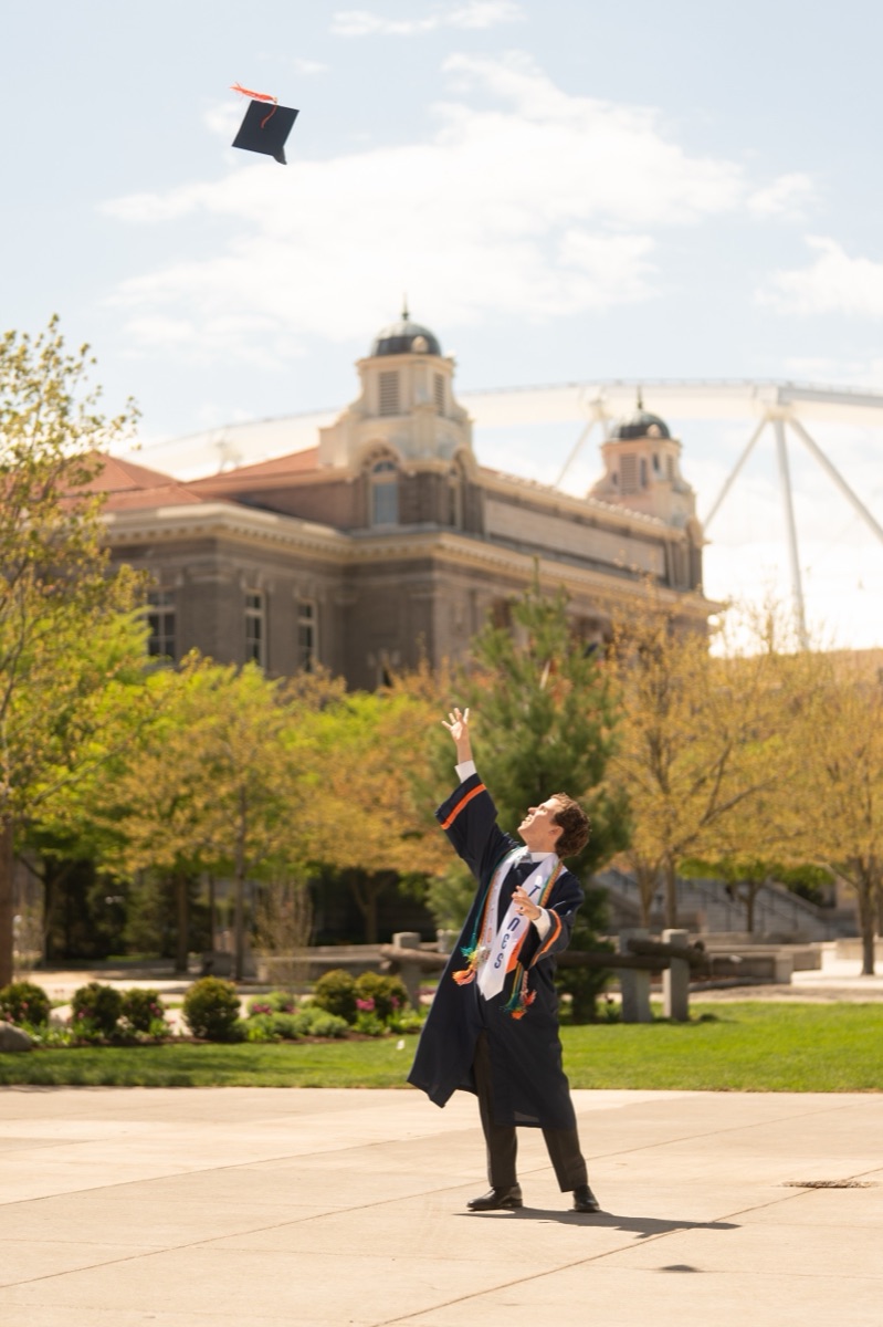 Graduate launching his cap in the air with campus bell towers and the stadium dome behind